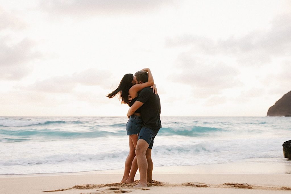 An image of a couple embracing while standing on the beach on Oahu.