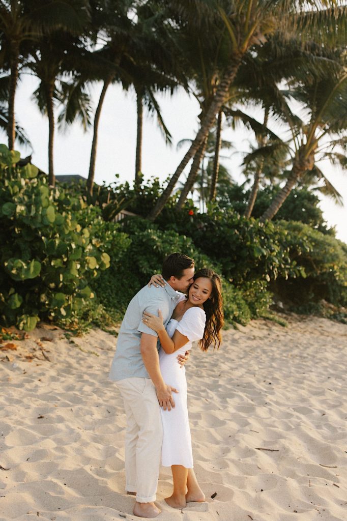 A couple smiles while embracing one another during their engagement session on a beach on the north shore of Oahu.