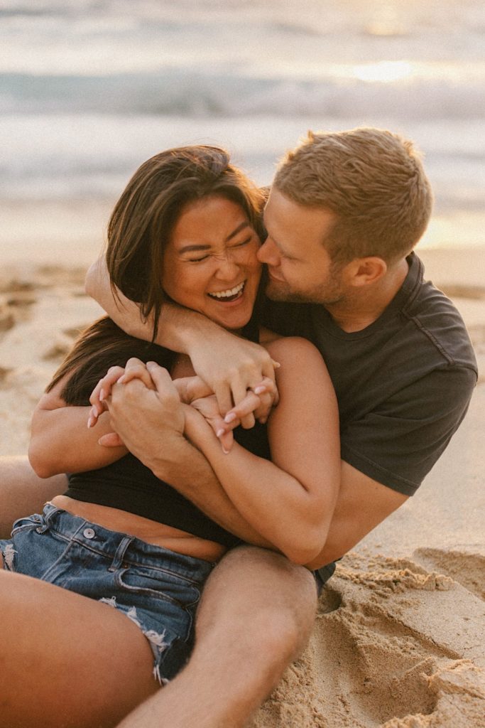 A close up image of a fiancé kisses his fiancées' neck while the hold one another on a Hawaii beach for their engagement session.