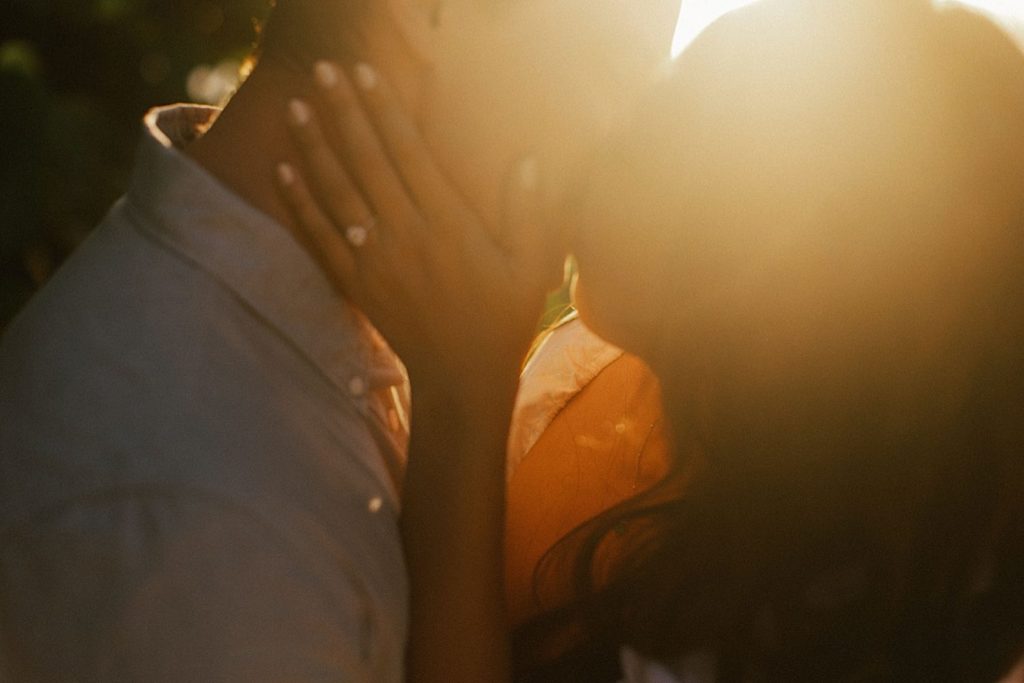 A couple kisses with the sun setting in the background during golden hour on Oahu.