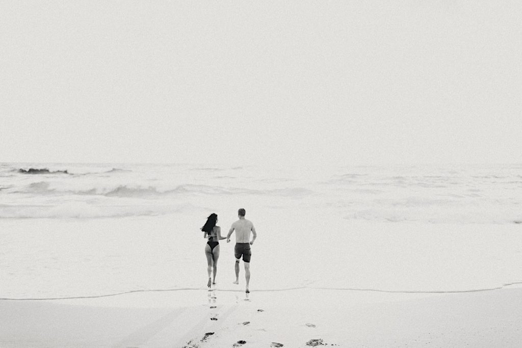 A couple runs into the water on the beach. 