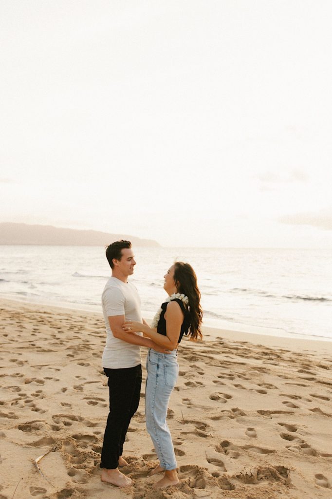 A couple stands holding one another during golden hour on Oahu.