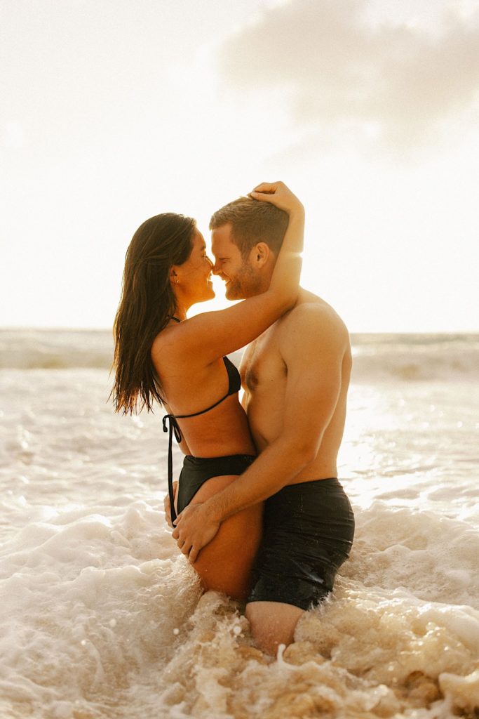 A couple holds one another and hugging in the shallow water of a beach in Hawaii