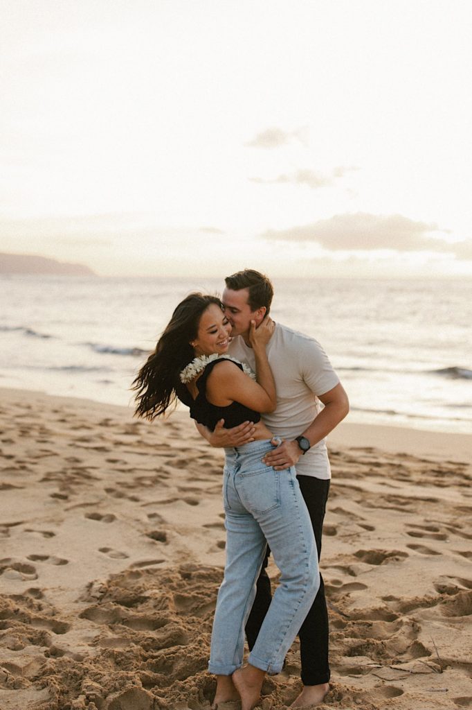 A couple embraces on a beach on Oahu during their engagement session.