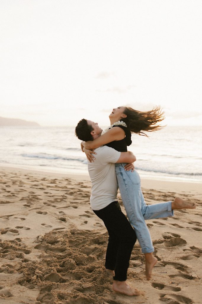 A couple embraces on a beach on Oahu during their engagement session.