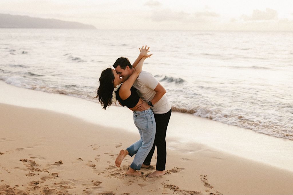 A couple hugs holding one another tight right on the shoreline of a beach on Oahu.  