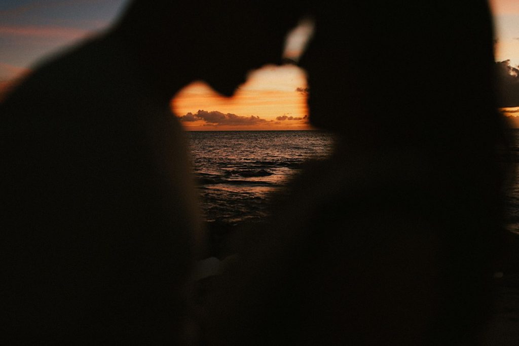 An engaged couple kisses while dancing during sunset on a beach in Oahu.