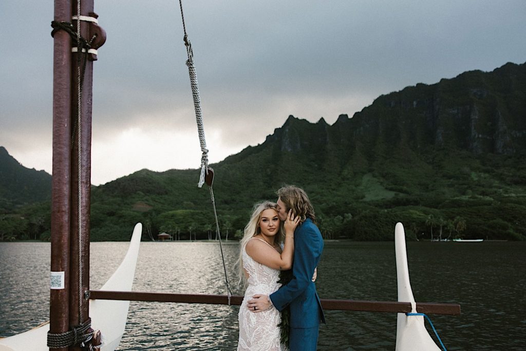 A couple holds one another on a boat on their wedding day during their newly wed portraits at Kualoa Ranch.
