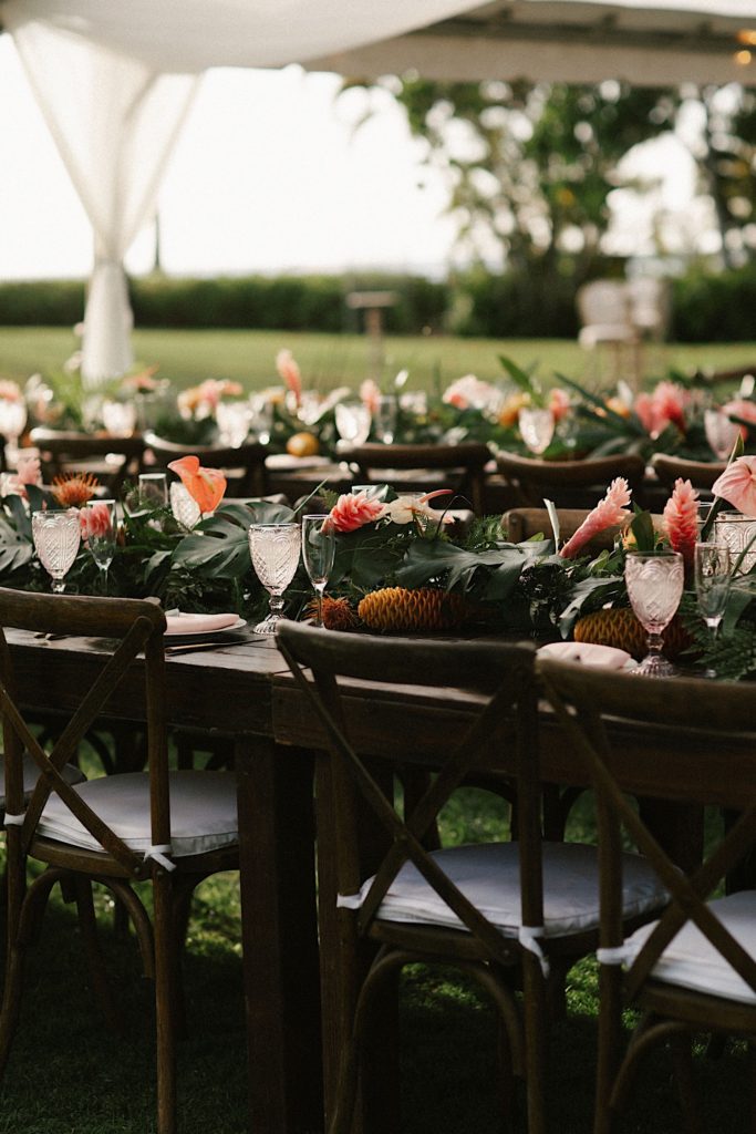 A tropical themed garland with pink flowers decorates the table for a wedding at Lanikūhonua in Hawaii.