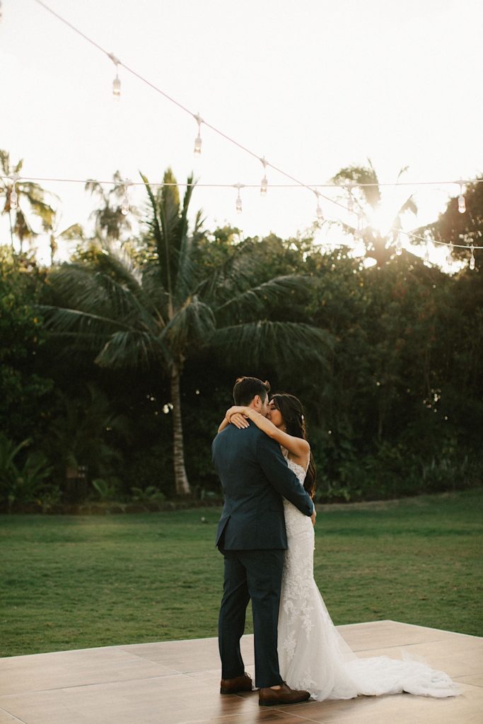 A couple kisses during their first dance overlooking palm trees during their wedding reception at Loulu Palm in Oahu.