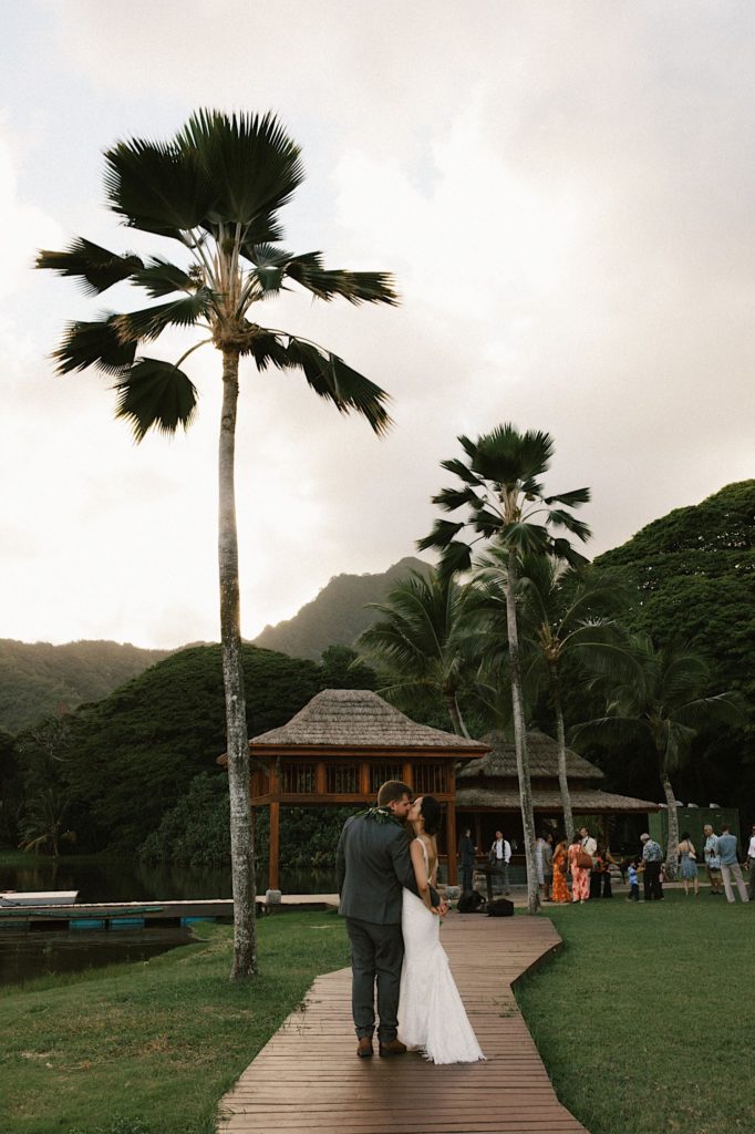 A married couple walks on a boardwalk towards their cocktail hour at Kualoa Ranch in Hawaii.