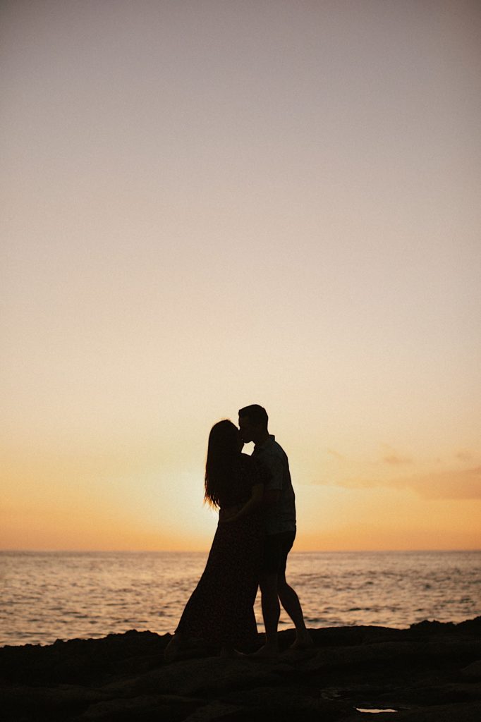 A silhouette of a couple standing in front of a sunset in Hawaii.