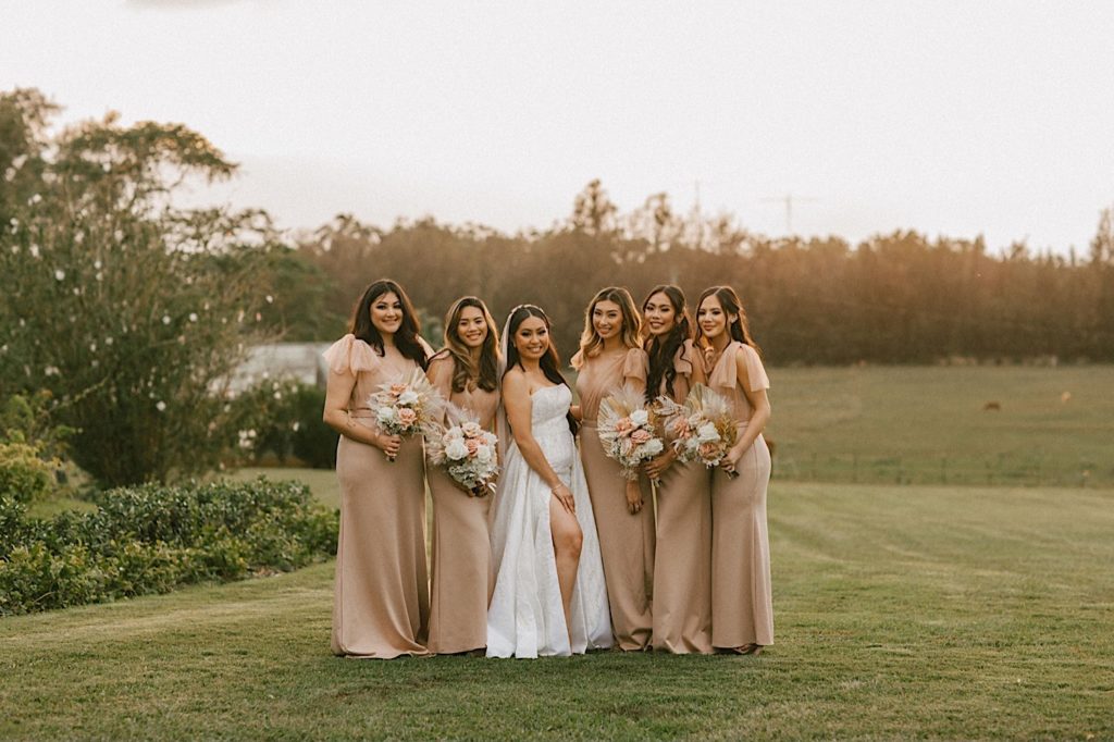 A bride stands with her wedding party during golden hour at their wedding reception in Sunset Ranch in Hawaii.