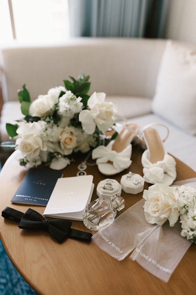 Photo of wedding details such as rings, shoes, vows and florals on a small table.