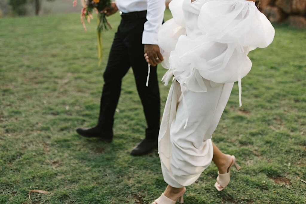 A waist down shot of a bride and groom walking hand in hand.