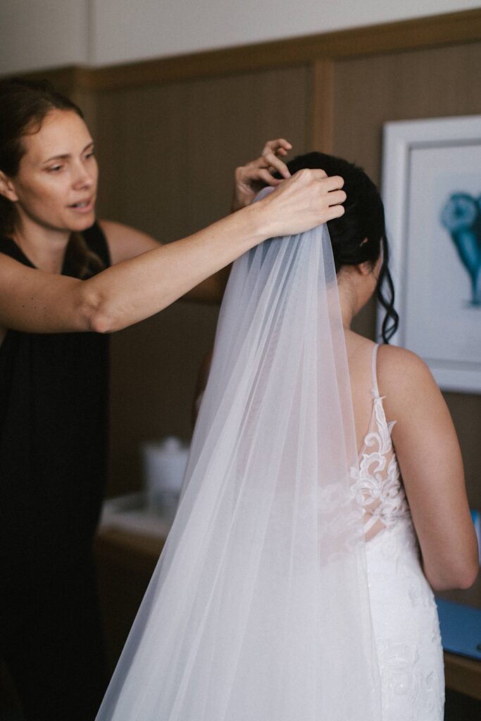 A woman helps put a brides veil on as she gets ready for her wedding day.