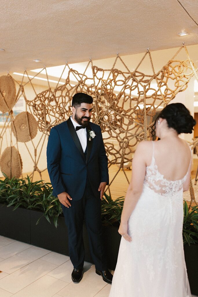 A groom smiles as he sees his bride on their wedding day for the first time with both of them in their wedding attire.