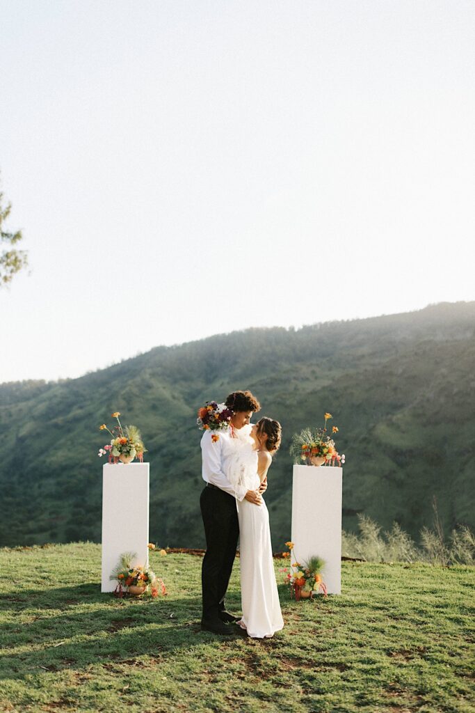 A bride and groom kiss at their ceremony space with mountains behind them.