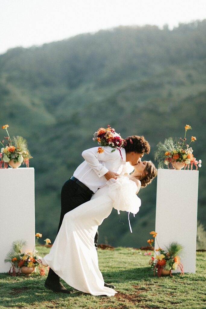 A bride and groom kiss at their ceremony space with mountains behind them.