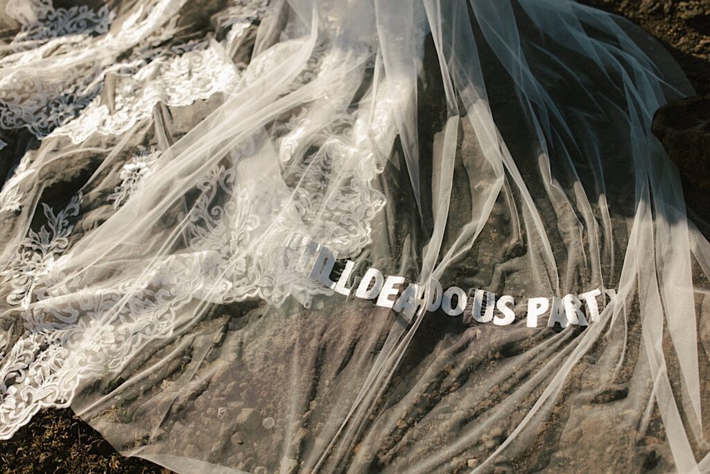 A sheer cloth with the words "till death do us part" on it is laid out over rocks.