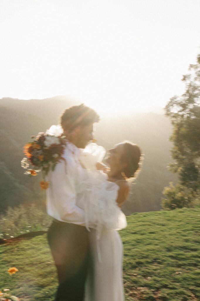 An out of focus shot of a bride and groom smiling with a bright Hawaiian sunset behind them