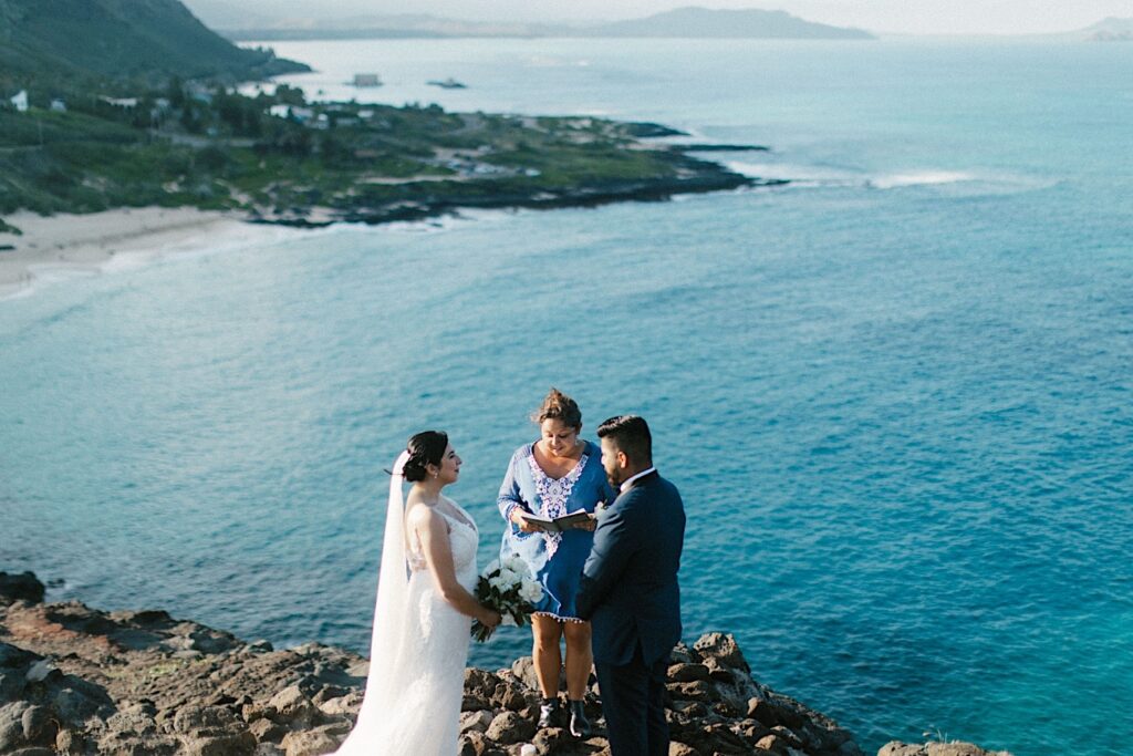 A bride and groom stand together and look at one another during their elopement ceremony on a cliff looking out over Makapuu Beach. 
