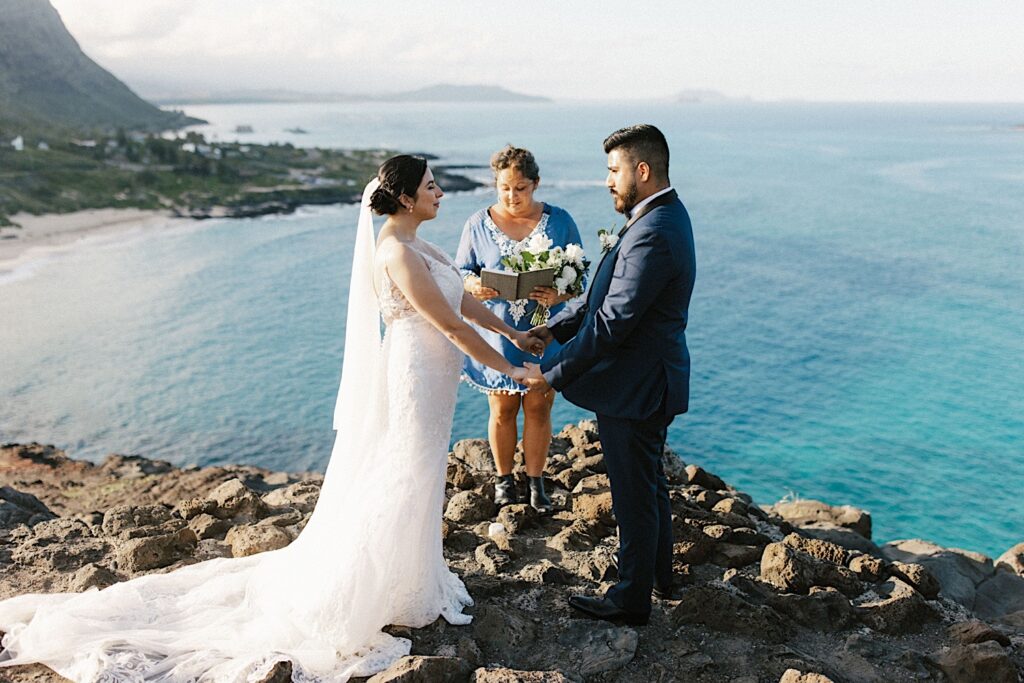 A bride and groom hold hands during their elopement ceremony on a cliff overlooking Makapuu Beach.