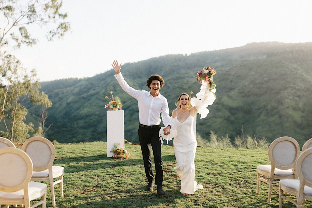 A bride and groom walk towards the camera with hands in the air celebrating their elopement at Waialua Valley Farms.