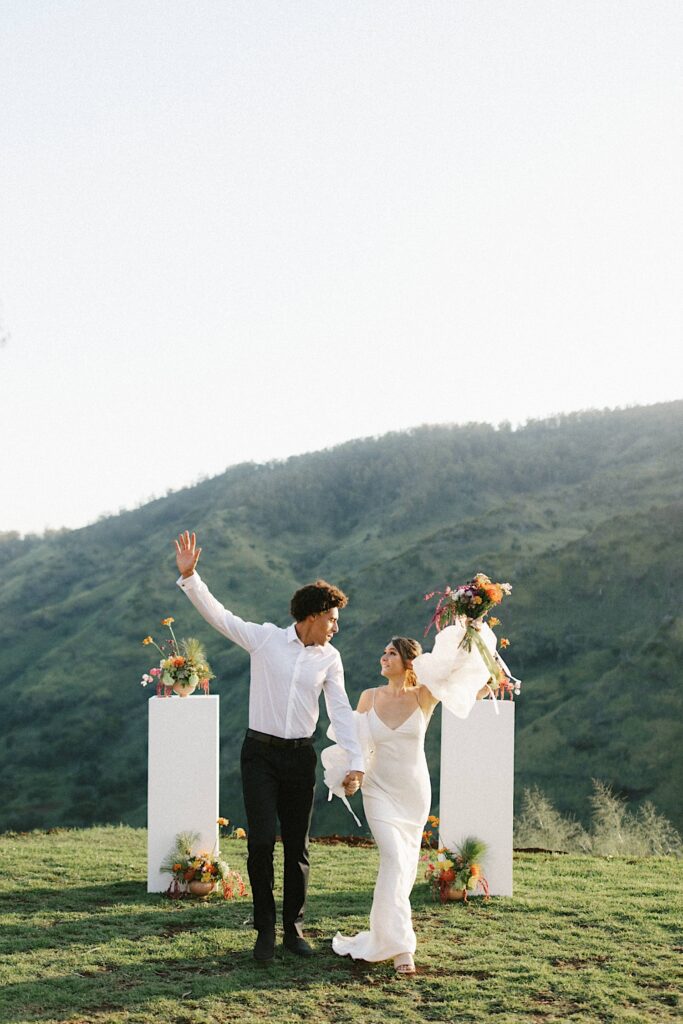 A bride and groom walk towards the camera with hands in the air celebrating their elopement.