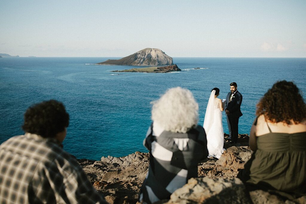 A family looks on as a bride and groom read their vows to one another during their elopement at Makapuu Lookout and Beach