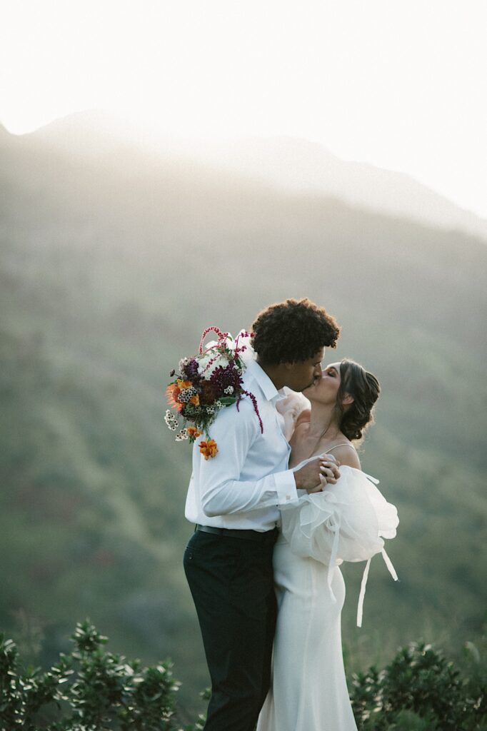 A bride and groom kiss one another after their elopement with mountains behind them.