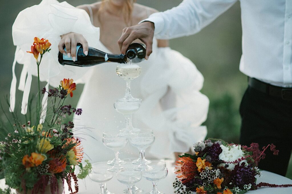 A bride and groom pour champagne over a tower of glasses at their wedding reception at Waialua Valley Farms.