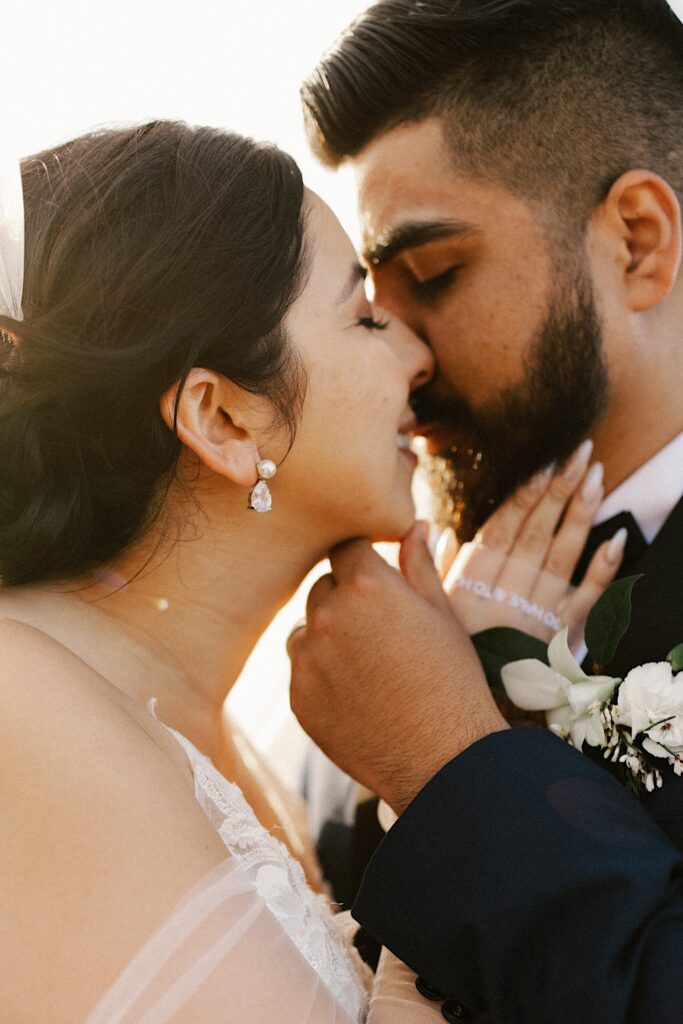 Closeup photo of a bride and groom about to kiss while the sun sets behind them.