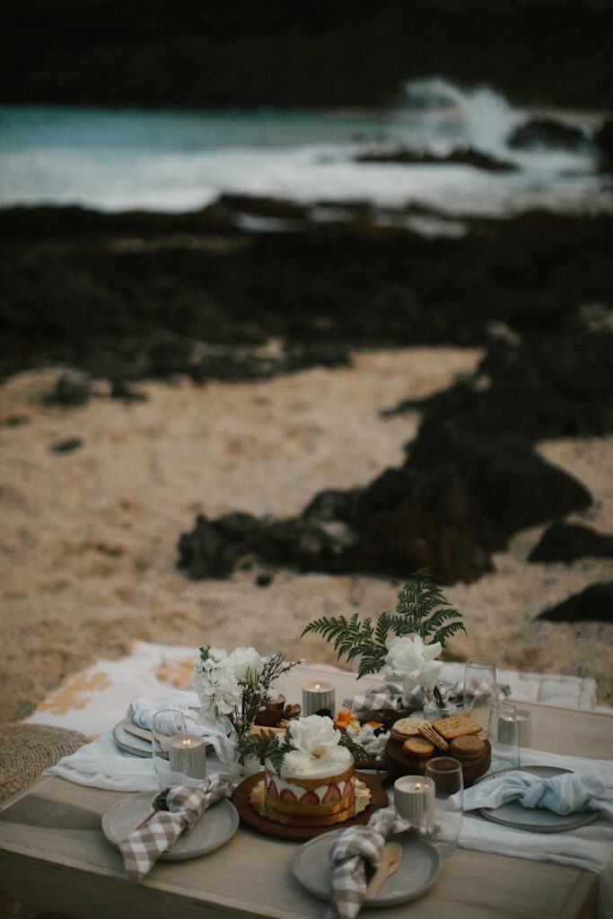 Detail photo of a picnic set up on a beach with snacks, florals and a cake for an elopement celebration.