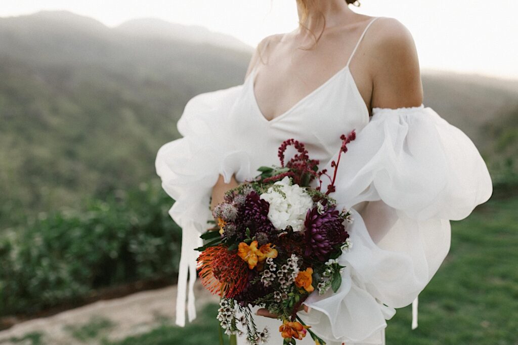 Portrait of a bride holding her bouquet with mountains behind her at Waialua Valley Farms
