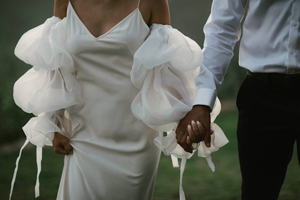 A bride and groom walk hand in hand during their wedding day.