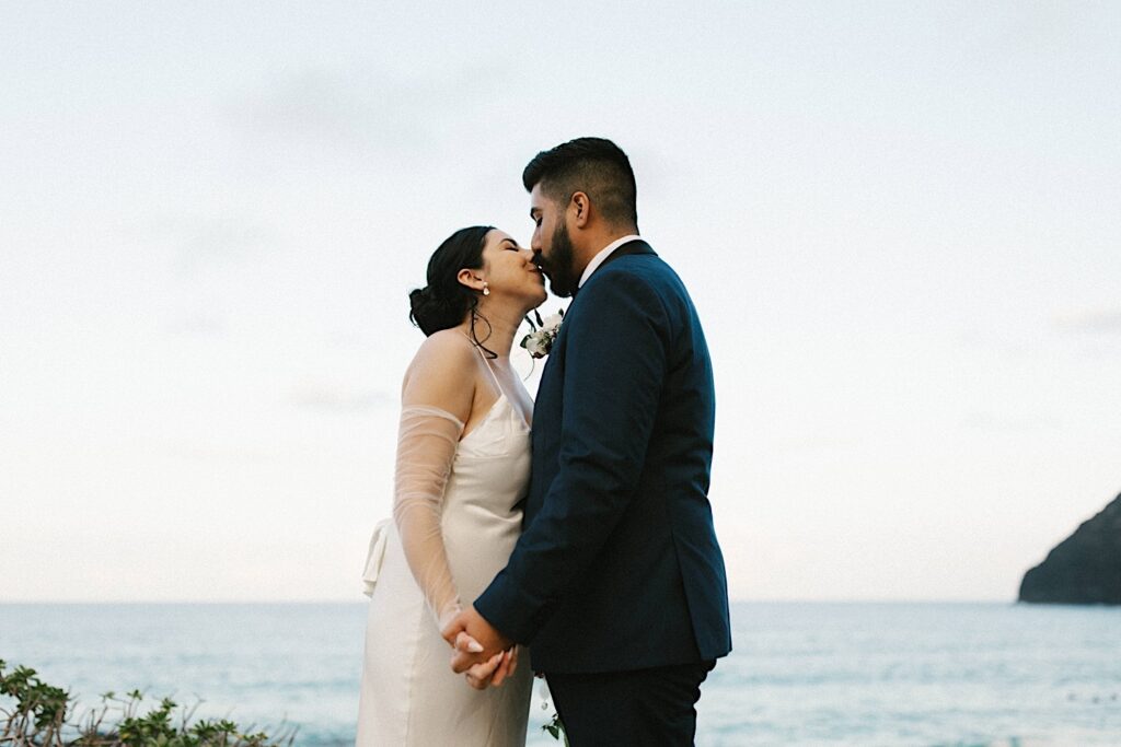 A bride and groom kiss while on Makapuu Beach in Hawaii after their elopement ceremony