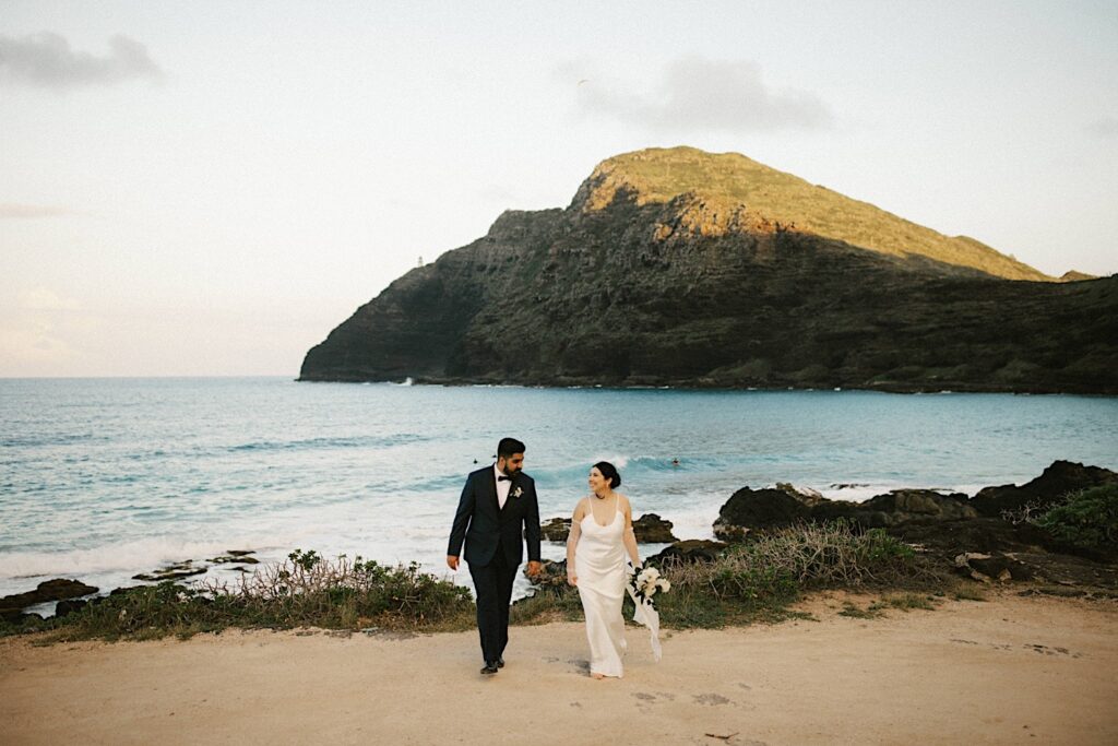 A bride and groom walk towards the camera and away from the ocean after their elopement on Makapuu Beach