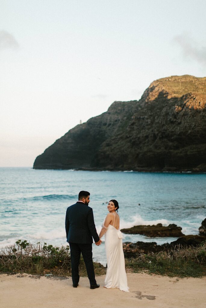 A bride and groom hold hands and smile while on Makapuu Beach in Hawaii