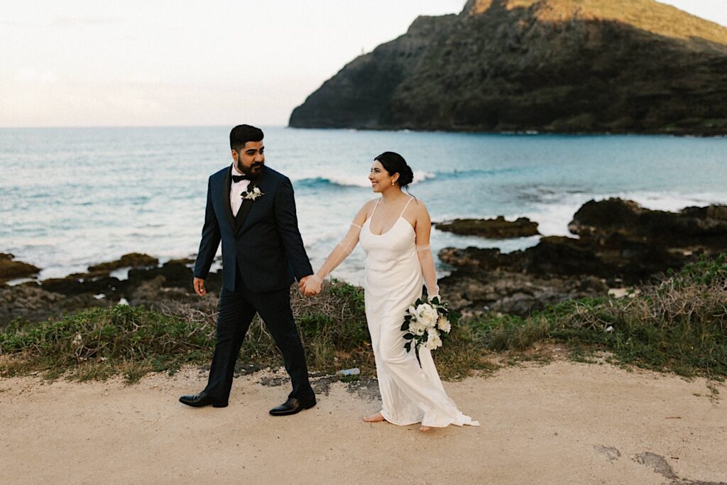 A bride and groom walk away from the ocean after their elopement on Makapuu Beach