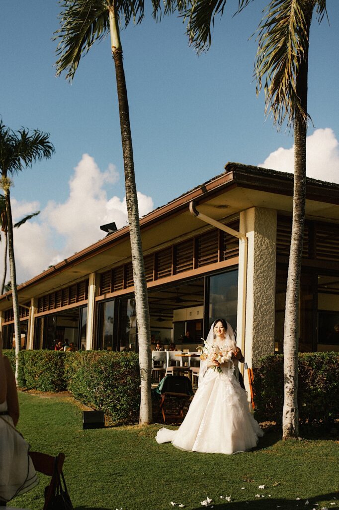 A bride in her wedding dress walks out of Beach House in Kauai towards her wedding ceremony.