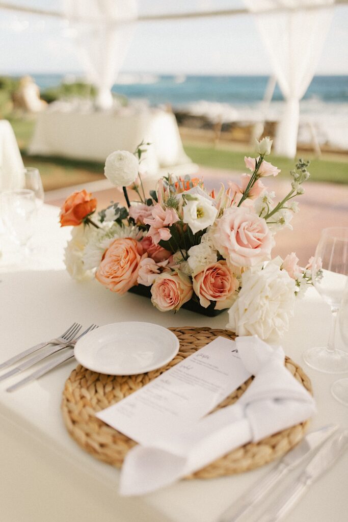 Detail photo of a placemat and florals set up for a wedding reception with the ocean in the background.