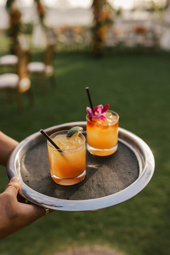 A closeup of two orange drinks on a platter being served at a wedding.