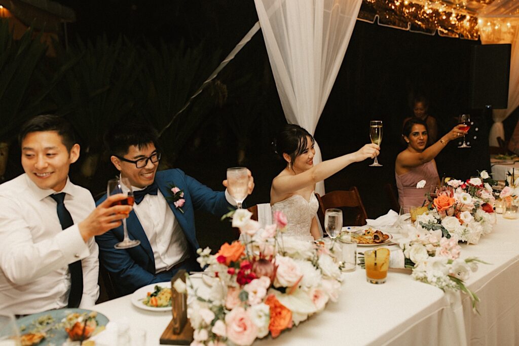 A bride, groom and their guests raise their glasses during a speech at their wedding reception.