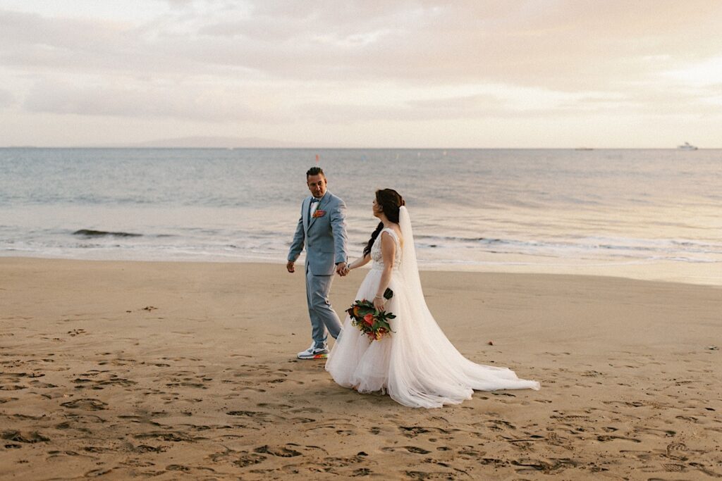 A newlywed couple walking along the beach of Maui after their wedding ceremony at Sugar Beach Events.