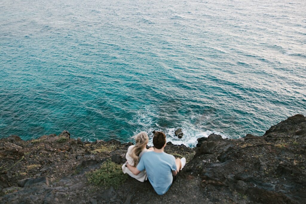 Before their proposal a couple sit atop a cliff on Makapuu Lookout in Hawaii and look down at the ocean below