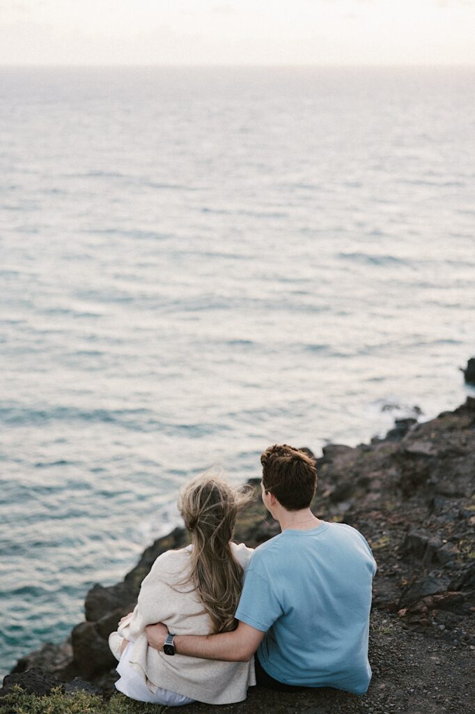 A couple embrace and look out over the ocean together while sitting atop Makapuu Lookout in Hawaii