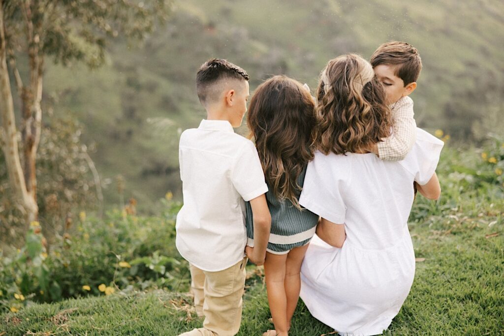 A group of four siblings hold hands and embrace while looking down a ravine during their family session on Oahu