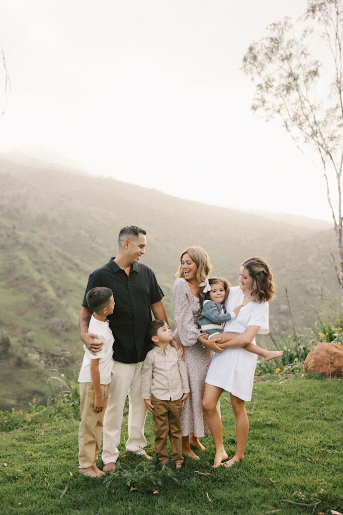 A couple stands and smiles with their four children with a mountain of Oahu in the background on a foggy day