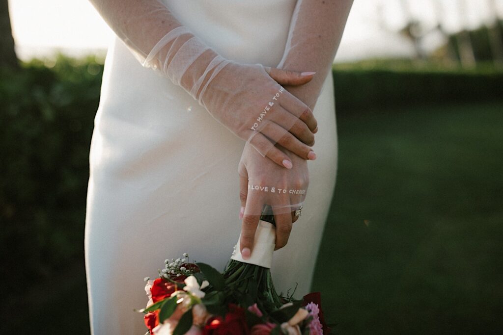 Close up photo of a bride with sheer sleeves on her dress that read "To have & to hold" and "To love & to cherish"